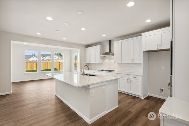 kitchen featuring stainless steel gas stovetop, wall chimney range hood, white cabinetry, and a center island with sink