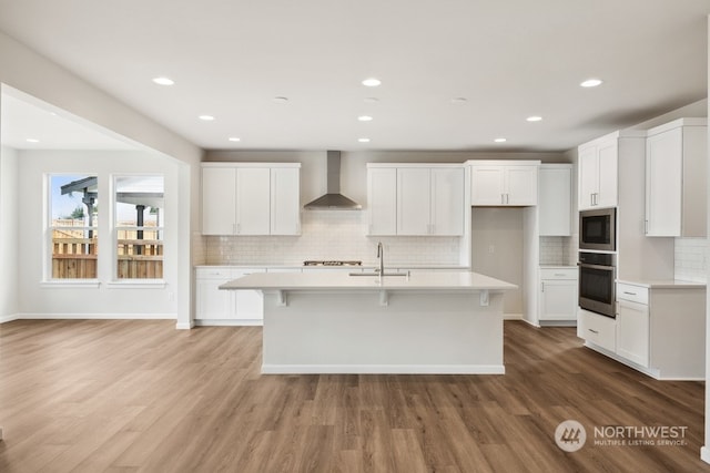 kitchen featuring white cabinets, appliances with stainless steel finishes, wall chimney exhaust hood, and an island with sink