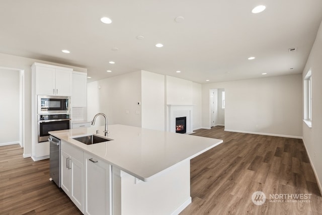 kitchen featuring white cabinetry, stainless steel appliances, an island with sink, sink, and hardwood / wood-style flooring