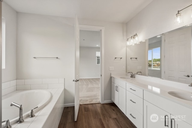 bathroom with hardwood / wood-style floors, tiled tub, and vanity