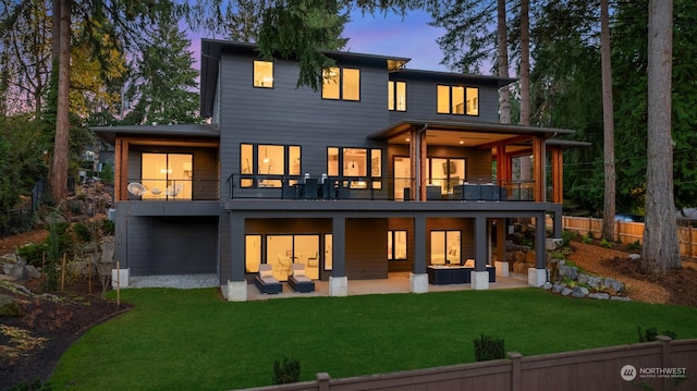 back house at dusk with an outdoor living space, a patio, a yard, and a balcony