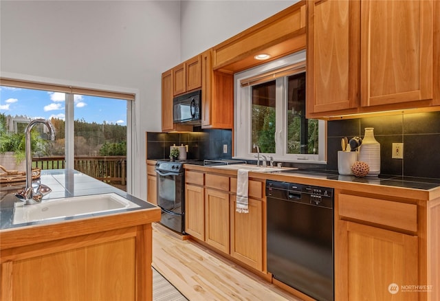 kitchen with decorative backsplash, sink, light hardwood / wood-style floors, and black appliances