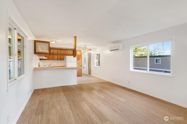 unfurnished living room featuring light wood-type flooring, a wall mounted air conditioner, and ceiling fan