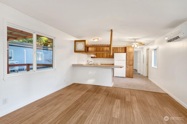 unfurnished living room with sink, ceiling fan, a wall mounted AC, and light hardwood / wood-style flooring