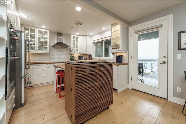 kitchen featuring light hardwood / wood-style floors, wall chimney range hood, white cabinets, and appliances with stainless steel finishes