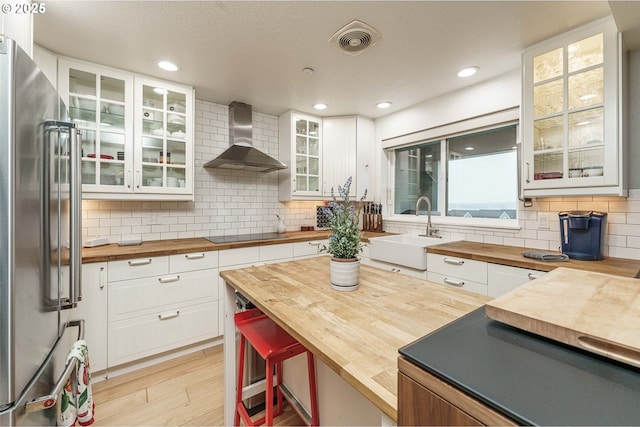 kitchen featuring white cabinets, wooden counters, high quality fridge, and wall chimney exhaust hood