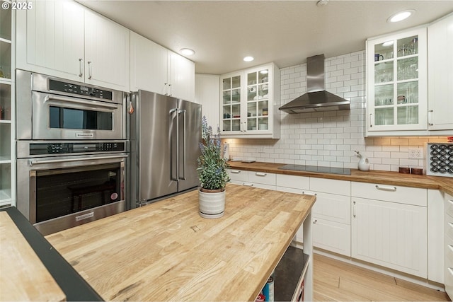 kitchen featuring wall chimney range hood, white cabinets, stainless steel appliances, and wood counters