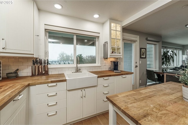 kitchen featuring decorative backsplash, wooden counters, sink, and white cabinetry