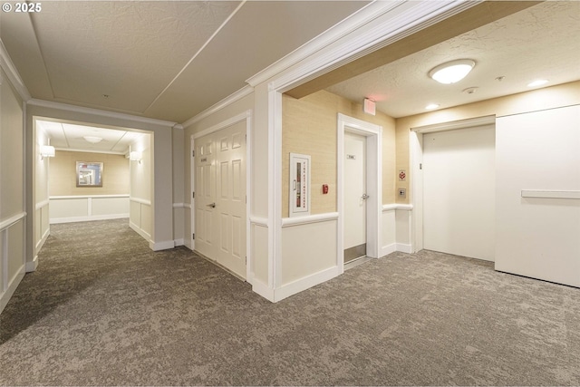 hall with a textured ceiling, crown molding, dark carpet, and elevator