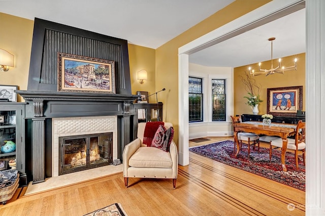 living area with a notable chandelier, hardwood / wood-style floors, and a tiled fireplace