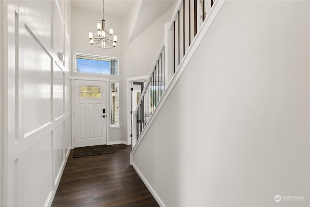 foyer entrance featuring dark hardwood / wood-style flooring, a towering ceiling, and an inviting chandelier