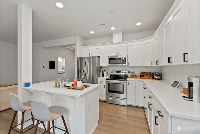 kitchen with light hardwood / wood-style floors, appliances with stainless steel finishes, tasteful backsplash, white cabinets, and a breakfast bar