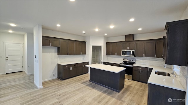 kitchen with appliances with stainless steel finishes, a center island, dark brown cabinets, light wood-type flooring, and a sink