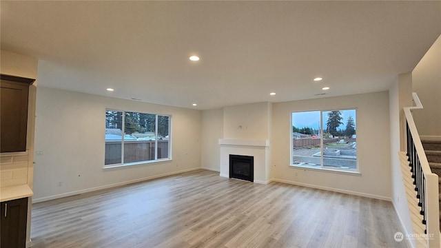 unfurnished living room with light wood finished floors, recessed lighting, stairs, and a glass covered fireplace