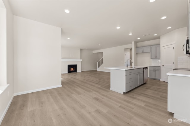 kitchen featuring appliances with stainless steel finishes, gray cabinetry, backsplash, a kitchen island with sink, and light hardwood / wood-style flooring