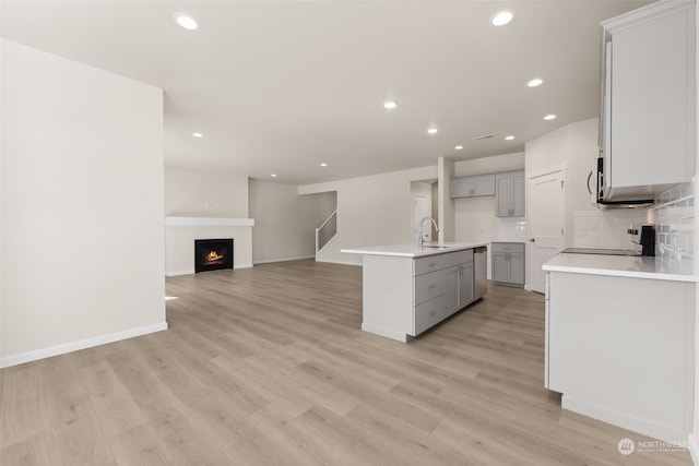 kitchen featuring gray cabinets, appliances with stainless steel finishes, a kitchen island with sink, tasteful backsplash, and light hardwood / wood-style floors