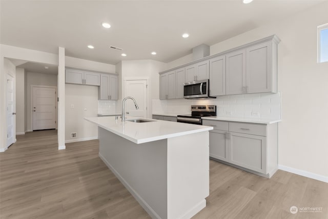 kitchen featuring appliances with stainless steel finishes, an island with sink, sink, gray cabinetry, and light wood-type flooring