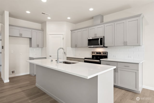 kitchen with appliances with stainless steel finishes, sink, a center island with sink, and light hardwood / wood-style flooring