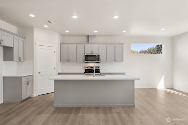 kitchen with stainless steel appliances, sink, an island with sink, and gray cabinetry