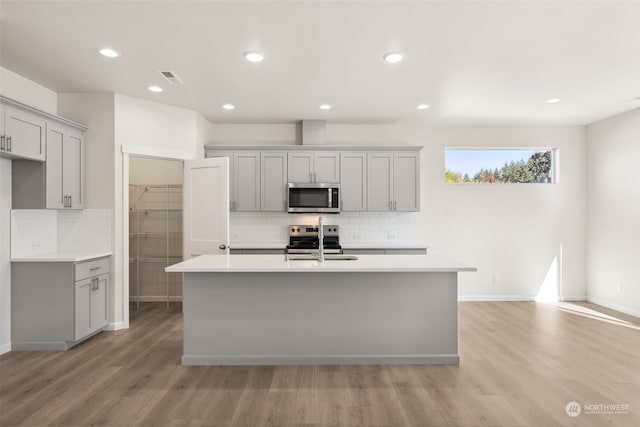 kitchen with appliances with stainless steel finishes, a center island with sink, and gray cabinetry