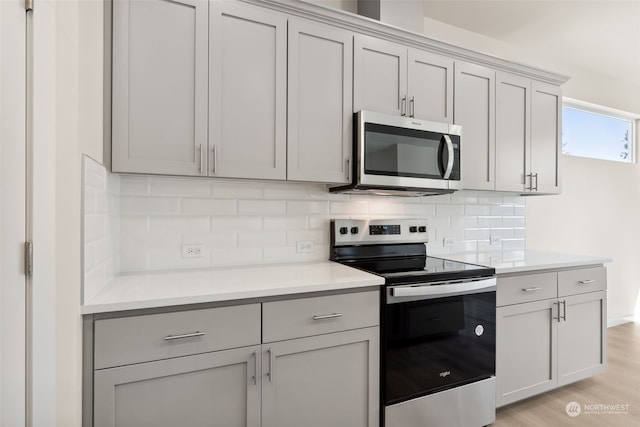 kitchen featuring appliances with stainless steel finishes, gray cabinets, light hardwood / wood-style floors, and decorative backsplash