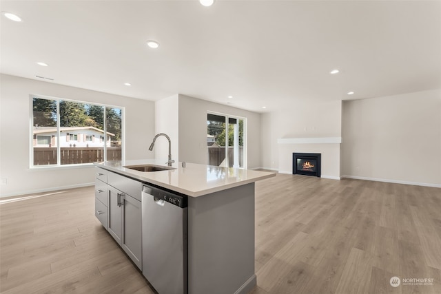 kitchen with gray cabinets, dishwasher, sink, light hardwood / wood-style floors, and a center island with sink