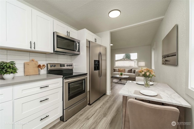 kitchen featuring a textured ceiling, white cabinets, stainless steel appliances, tasteful backsplash, and light hardwood / wood-style flooring