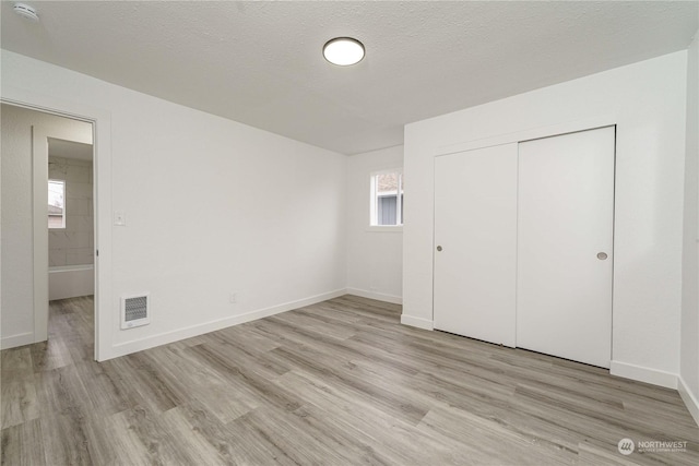 unfurnished bedroom with a textured ceiling, a closet, and light wood-type flooring