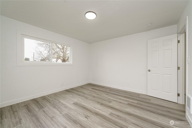 spare room with a textured ceiling and light hardwood / wood-style flooring