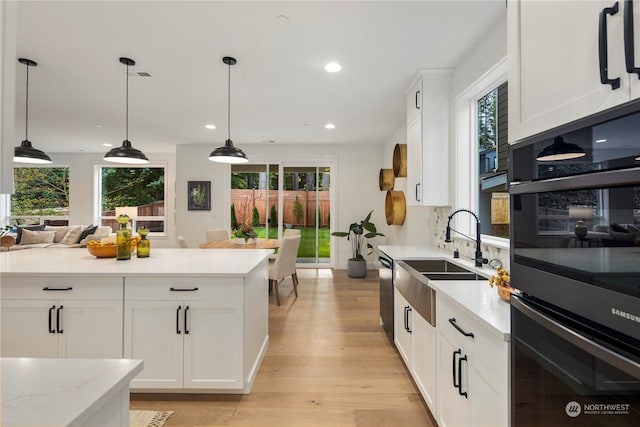 kitchen featuring decorative light fixtures, white cabinets, plenty of natural light, and sink