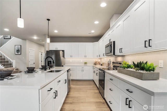 kitchen with white cabinets, decorative backsplash, light wood-style flooring, appliances with stainless steel finishes, and pendant lighting