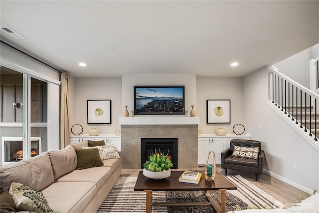 living area with stairs, wood finished floors, a tile fireplace, and visible vents