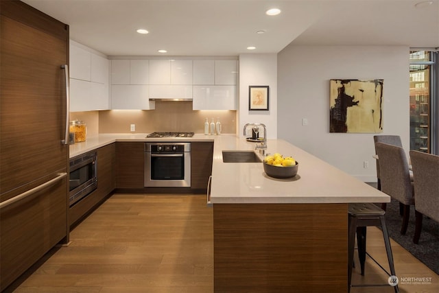 kitchen featuring a kitchen bar, sink, white cabinets, light hardwood / wood-style flooring, and stainless steel appliances