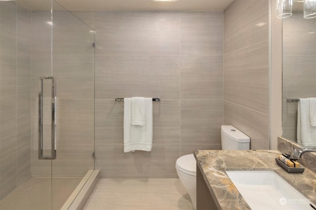 bathroom with toilet, vanity, an enclosed shower, and tile walls