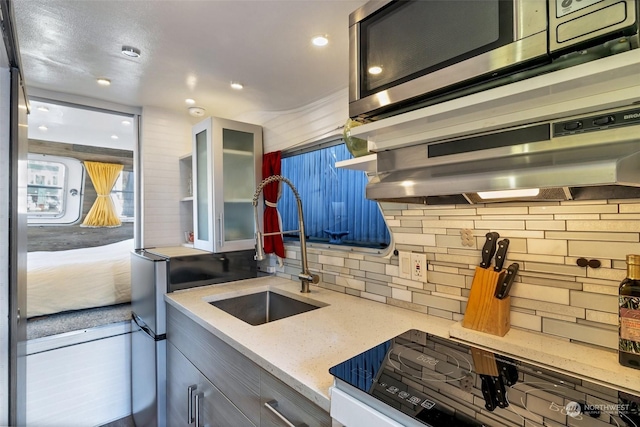 kitchen featuring sink, tasteful backsplash, light stone counters, stove, and ventilation hood