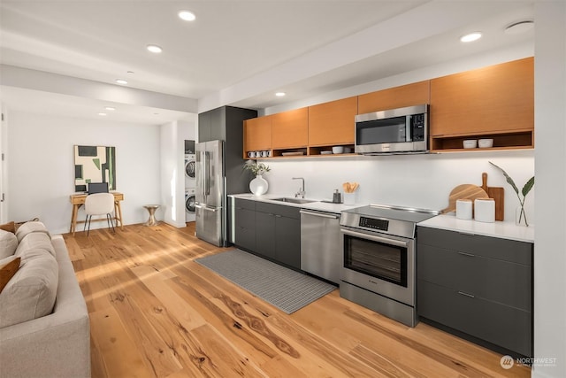 kitchen with stacked washing maching and dryer, sink, stainless steel appliances, and light hardwood / wood-style flooring