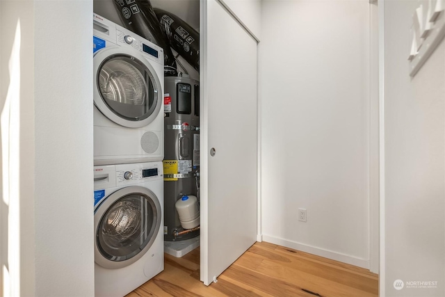 washroom with stacked washer / drying machine, water heater, and light hardwood / wood-style flooring