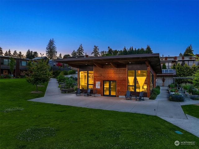 back house at dusk featuring a yard and a patio