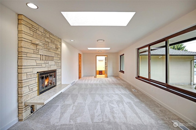 unfurnished living room with light carpet, a skylight, and a stone fireplace