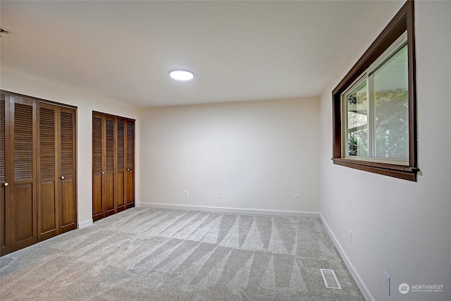 unfurnished bedroom featuring two closets and carpet