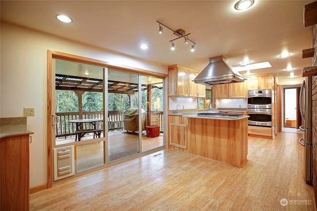 kitchen with appliances with stainless steel finishes, island exhaust hood, light brown cabinetry, kitchen peninsula, and light wood-type flooring