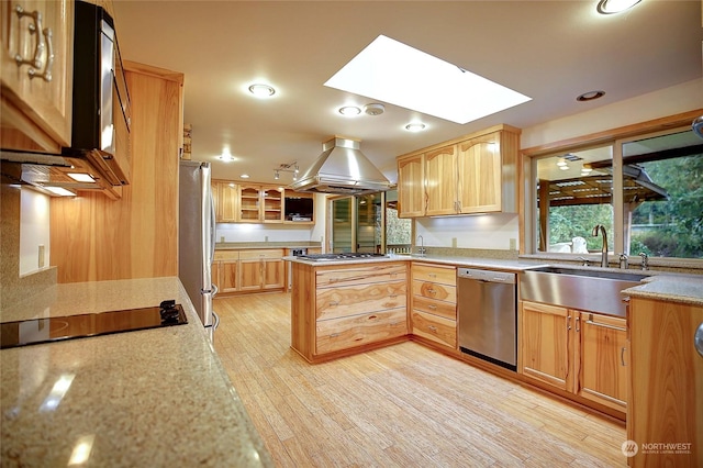 kitchen featuring a skylight, island range hood, appliances with stainless steel finishes, light hardwood / wood-style flooring, and sink