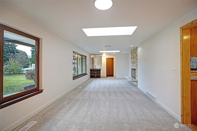 unfurnished living room featuring light carpet, a skylight, and a stone fireplace