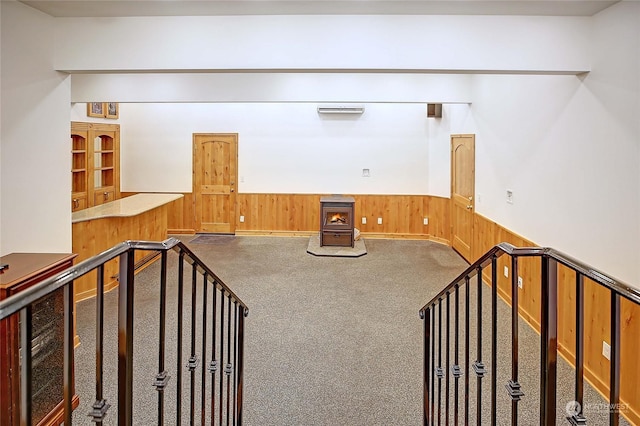 unfurnished living room with carpet floors, a wood stove, and wooden walls