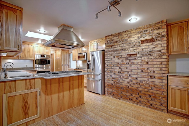 kitchen with light hardwood / wood-style floors, sink, island exhaust hood, stainless steel appliances, and brick wall