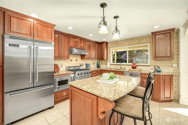 kitchen with a kitchen island, decorative light fixtures, built in appliances, sink, and a kitchen breakfast bar