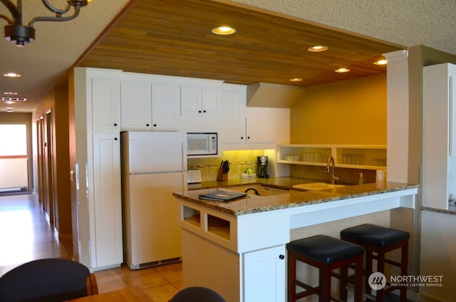 kitchen with white appliances, white cabinets, dark stone counters, sink, and kitchen peninsula