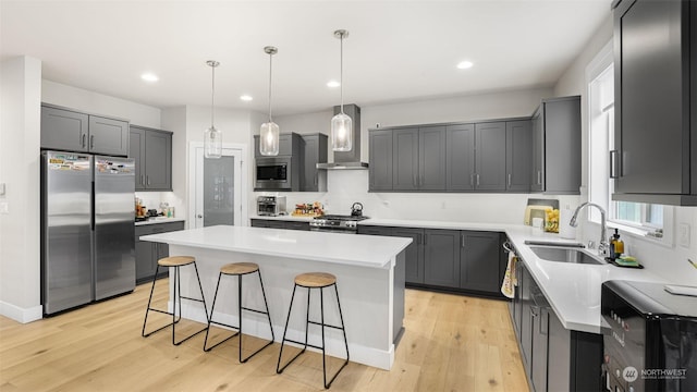 kitchen with wall chimney range hood, a kitchen island, sink, appliances with stainless steel finishes, and a breakfast bar area