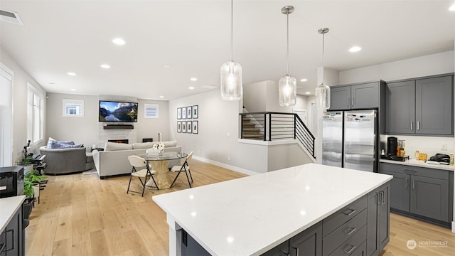 kitchen with light hardwood / wood-style floors, gray cabinetry, decorative light fixtures, stainless steel refrigerator, and a center island