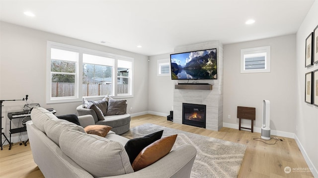 living room featuring a wealth of natural light, a tile fireplace, and light hardwood / wood-style floors